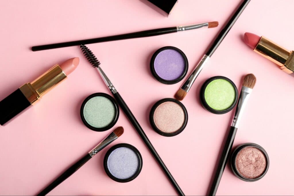 Several colors of eyeshadow and cosmetics brushes on a pink background