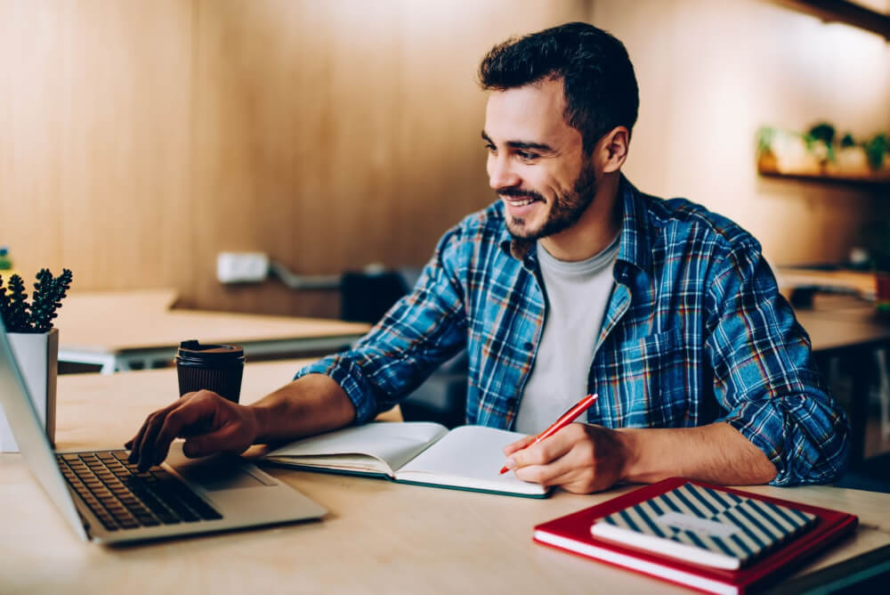 A man sits at a laptop while working on a content calendar for a company.