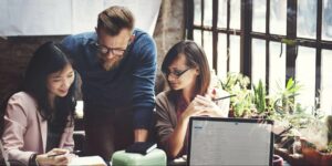 Three business bloggers gather around a notebook to discuss their blogging strategy.
