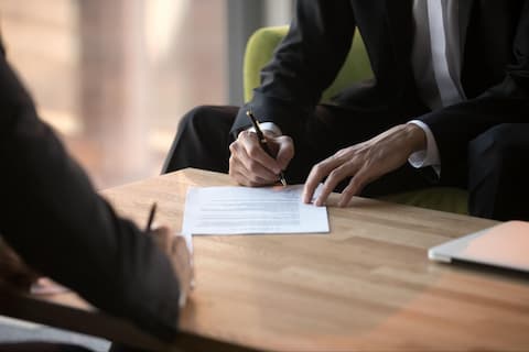 A man in a suit writing on a piece of paper across from a member of a digital marketing agency for franchises.