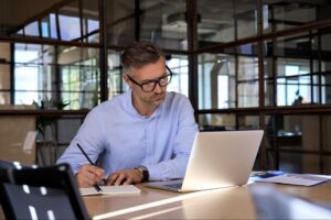 A man optimizing performance max campaigns on a laptop and writing notes.